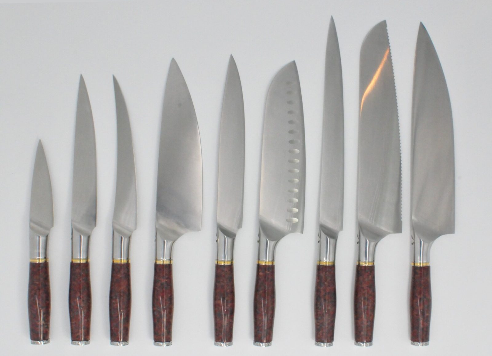 https://www.craftstoneknives.com/wp-content/uploads/2019/09/9-Knife-Set-with-a-Red-Granite-Handle-a-Garnet-Colored-Cubic-Zirconia-Stone-at-the-Back-of-the-Knife-and-Brass-and-Stainless-Steel-Decorative-Rings.jpg